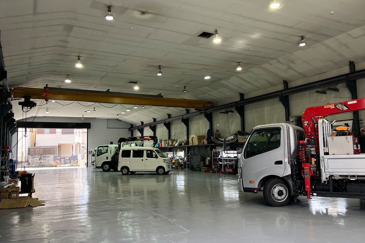 トラックやクレーン車など様々な車両が並ぶ広い整備工場内