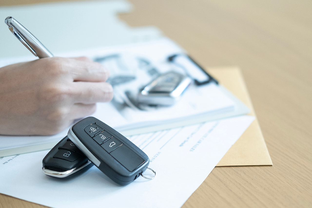 机の上に置かれた車のスマートキーと書類にペンで記入する手元