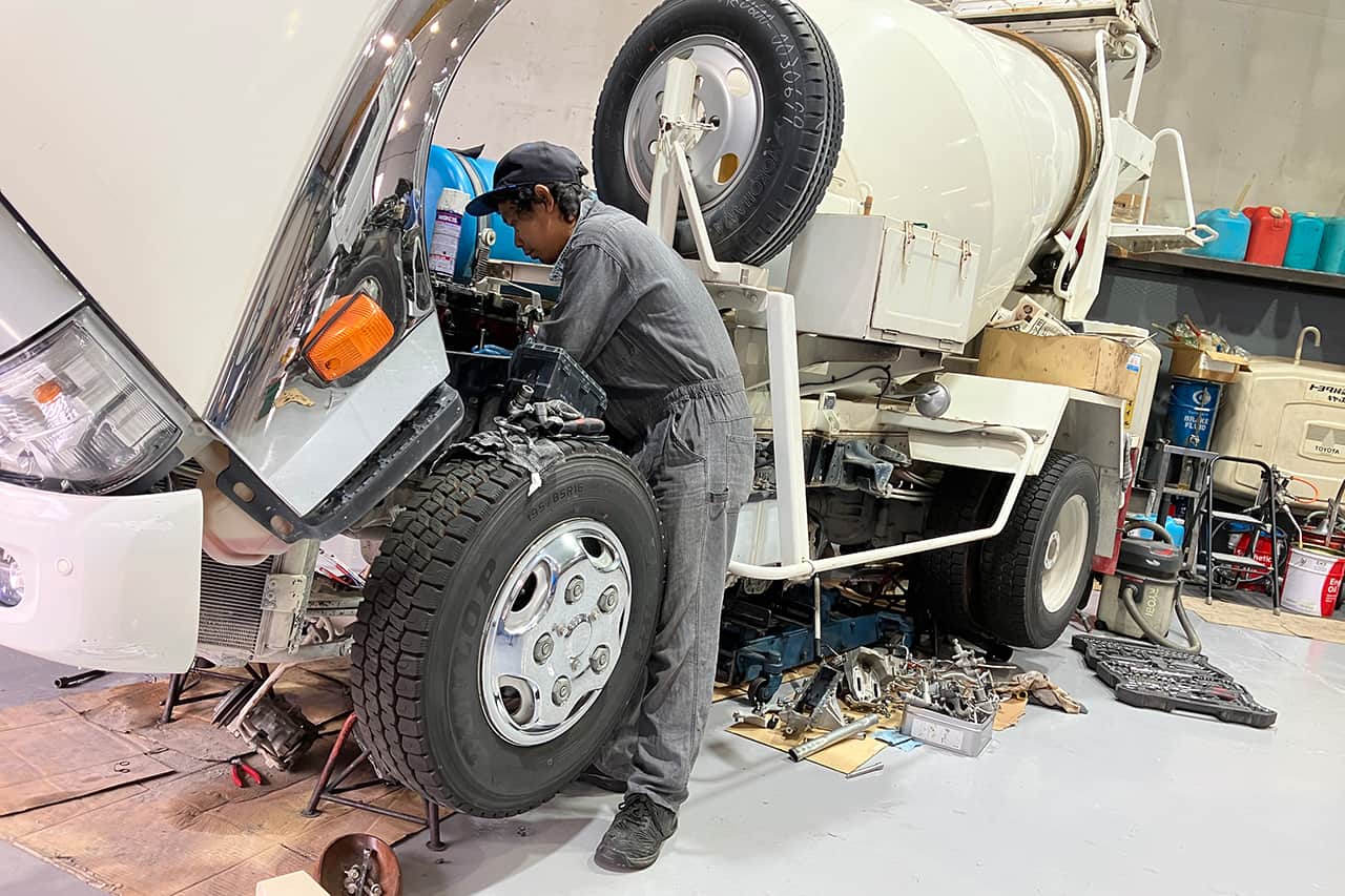 ミキサー車の前輪付近で整備作業を行う作業員